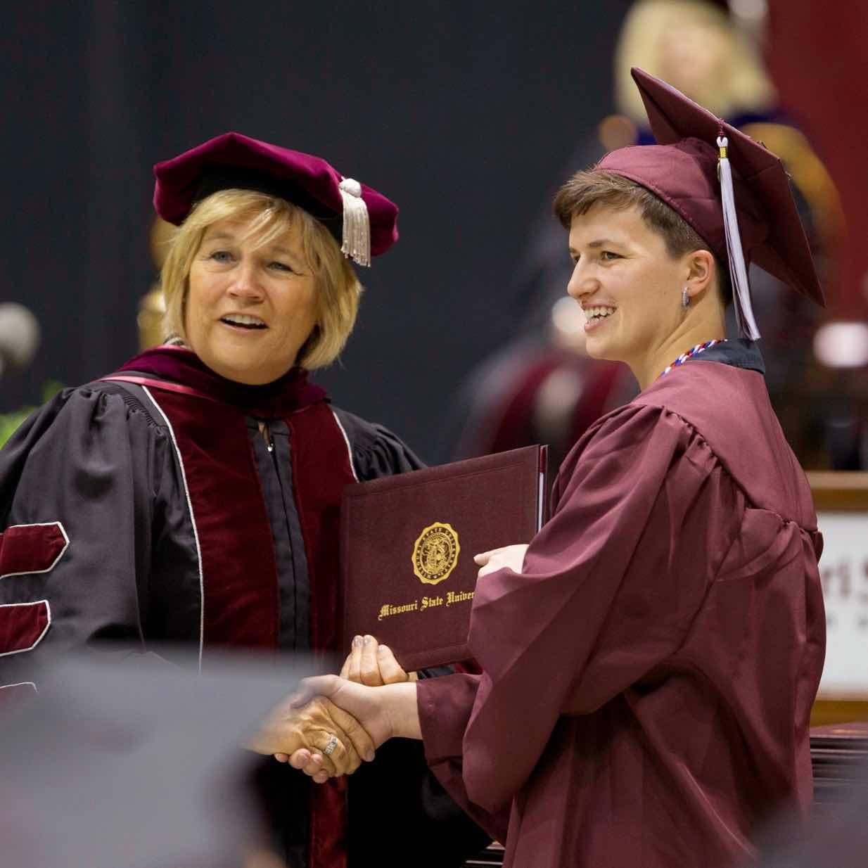 Graduating student shakes hand with faculty memeber while accepting diploma