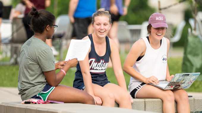 Three female students laughing and studying while dangling their feet in a fountain