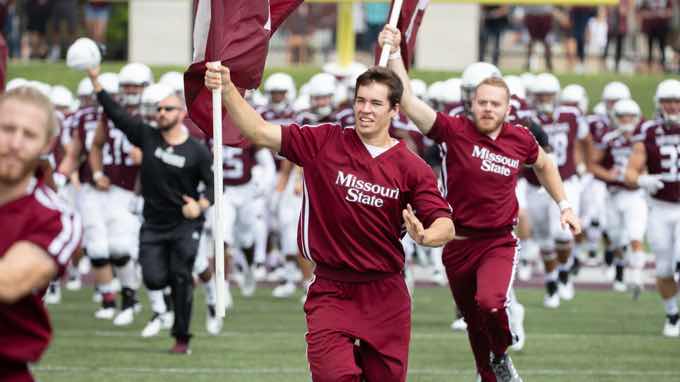 Male cheerleaders running with flags down football field