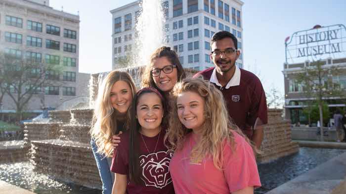 Group of students standing in front of a fountain with an urban background