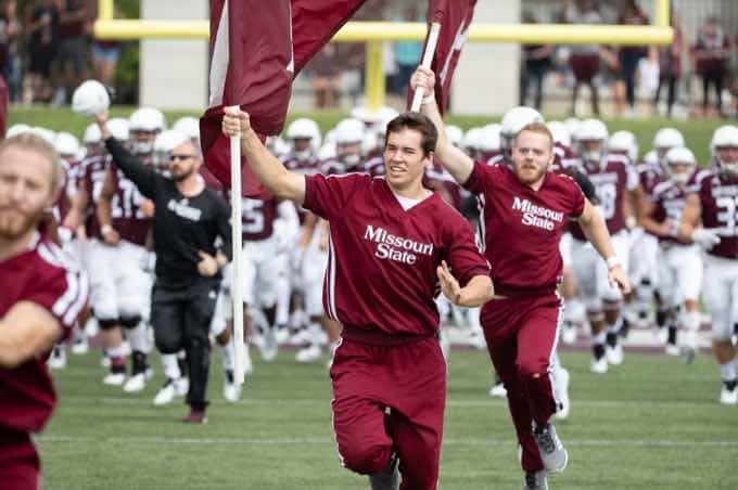 Male cheerleaders running with flags down football field
