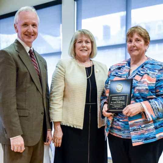 Linda Wulff-Risner holds the Governor's Award for Excellence, surrounded by the Dean of Academic Affairs and First Lady of Missouri